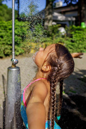 Pretty girl takes shower on the beach in the summer camp, refreshing in cold water, enjoying summer vacation on the sea resort, family travel and recreationの写真素材