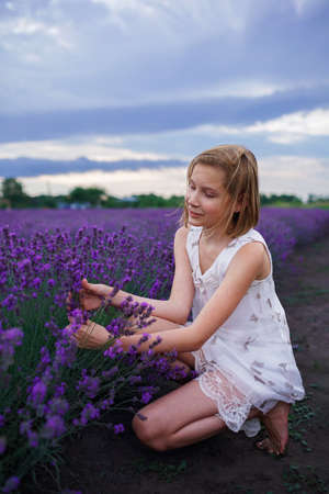 Teenage girl enjoys the scenery of lavender field. Dreamy teenager walking among purple flowers on the beautiful sunset. Calm landscape, escape to beauty of nature, summer travel and vacationの写真素材