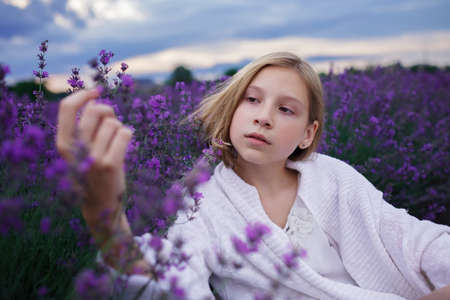 Teenage girl enjoys the scenery of lavender field. Dreamy teenager walking among purple flowers on the beautiful sunset. Calm landscape, escape to beauty of nature, summer travel and vacationの写真素材