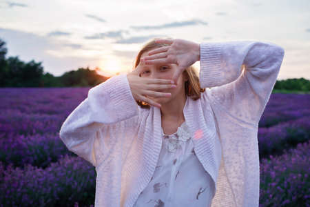 Young girl put her fingers before face like photo frame, she enjoys lavender field. Happy teenager among purple flowers at beautiful sunset. Calm landscape, beauty of nature, summer travel, vacationの写真素材