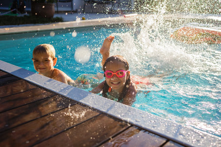 Cheerful children in googles laughing while playing in swimming pool at sunny day, refreshing at heat weather, active vacation and healthy lifestyle, happy summertimeの写真素材