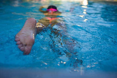 Girl in swimming suit and goggles training swim at pool in summer camp. Refreshing at heat weather,...