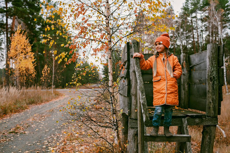 Happy ten years girl in orange coat and hat walks and plays in handmade wooden house in the fall park. Autumn vibes, outdoor lifestyle. Hello autumn, active weekend on fresh airの写真素材