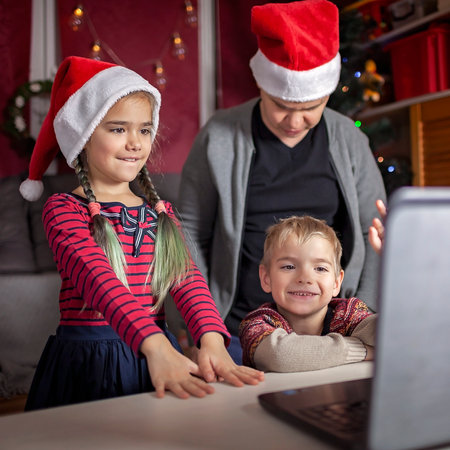 Safe online Christmas celebration. Happy family in Santa red hats celebrating with friends virtually via internet and notebook. Video call. Stay home, distant holiday, lifestyleの写真素材