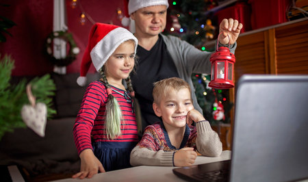 Safe online Christmas celebration. Happy family in Santa red hats celebrating with friends virtually via internet and notebook. Video call. Stay home, distant holiday, lifestyleの写真素材