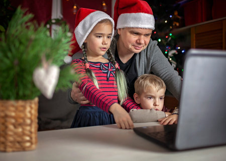 Safe online Christmas celebration. Happy family in Santa red hats celebrating with friends virtually via internet and notebook. Video call. Stay home, distant holiday, lifestyleの写真素材