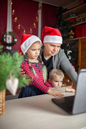 Safe online Christmas celebration. Happy family in Santa red hats celebrating with friends virtually via internet and notebook. Video call. Stay home, distant holiday, lifestyleの写真素材