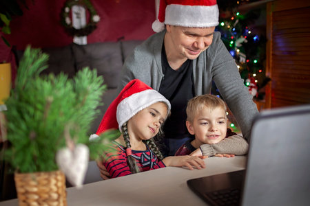 Safe online Christmas celebration. Happy family in Santa red hats celebrating with friends virtually via internet and notebook. Video call. Stay home, distant holiday, lifestyleの写真素材