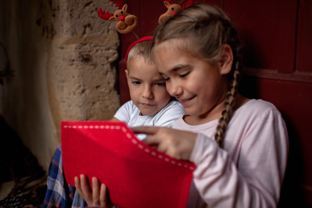 Happy siblings wearing in fun hat write a letter for Santa and dreamily waiting for gifts on Christmas Eve. Winter holidays in different places, Noel traditionの写真素材
