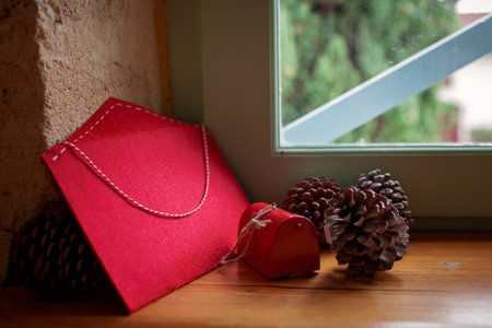 A fat envelope for letters to Santa Claus, large beautiful fir cones and a small decorative mailbox as Christmas decor lie on the windowsill in an old house. Seasonal holiday is comingの写真素材