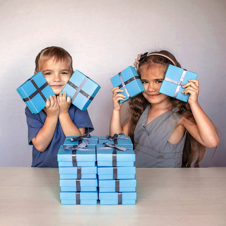 Cute little girl with her smaller brother near a huge pile of blue gift boxes with gray ribbons over white studio backgroundの写真素材
