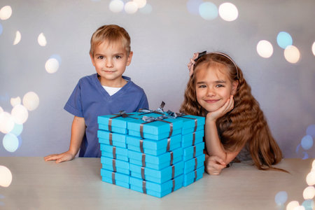 Cute little girl with her smaller brother near a huge pile of blue gift boxes with gray ribbons over white studio backgroundの写真素材
