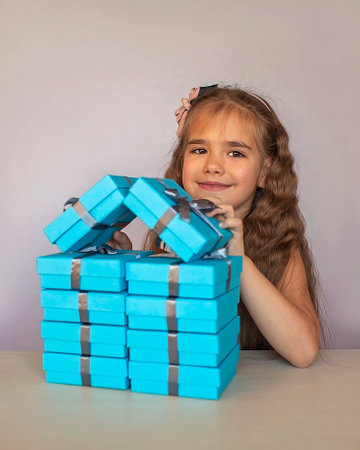 Cute little girl near a huge pile of blue gift boxes formed like a house over white studio background, she dreaming about new apartment, season holiday wish conceptの写真素材