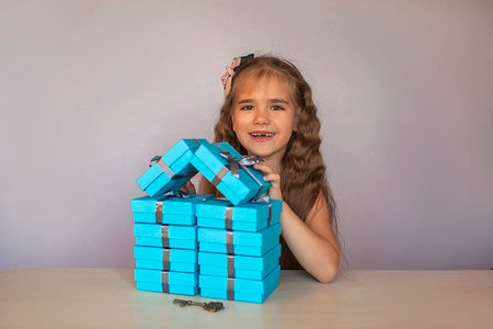 Cute little girl near a huge pile of blue gift boxes formed like a house over white studio background, she dreaming about new apartment, season holiday wish conceptの写真素材