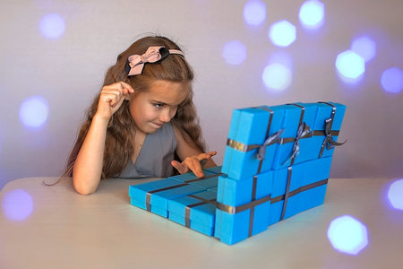 Cute little girl near a huge pile of blue gift boxes formed like a laptop over white studio background, she dreaming about laptop, season holiday wish conceptの写真素材