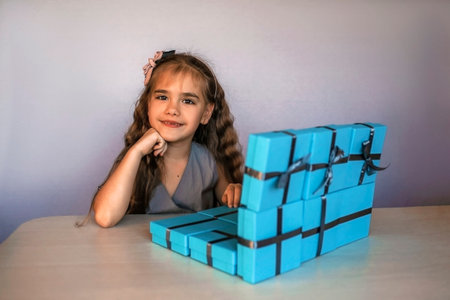 Cute little girl near a huge pile of blue gift boxes formed like a laptop over white studio background, she dreaming about travel, season holiday wish conceptの写真素材