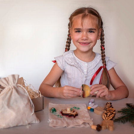 Cute preschool girl doing craft wrapping for festive gifts with stamp printing technique, printing home textile with wooden printing block, zero waste and craft for holiday conceptの写真素材