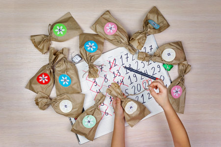Cute girl waiting for Christmas, opening paper bag with sweets and crossing out every day in calendar, family winter holidaysの写真素材