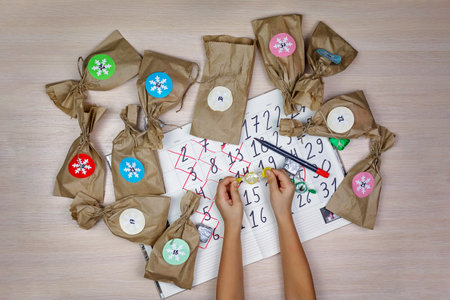 Cute girl waiting for Christmas, opening paper bag with sweets and crossing out every day in calendar, family winter holidaysの写真素材
