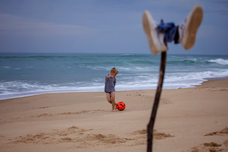 A small football fan barefoot repeats the tricks of his idol right on the ocean. Football everywhere. Sport, soccer, fandom. The football festival is comingの写真素材