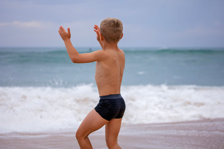 A boy of 7-8 years old sits on the ocean shore with his arms open towards the wind and waves. Storm on the ocean in summer. The concept of freedom, courage and challenge. Place for textの写真素材