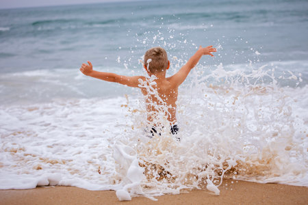 A boy of 7-8 years old sits on the ocean shore with his arms open towards the wind and waves. Storm on the ocean in summer. The concept of freedom, courage and challenge. Place for textの写真素材
