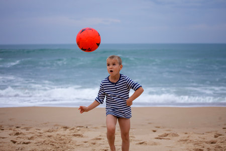 A small football fan barefoot plays football just on the band of ocean. Football everywhere. Sport, soccer, fandom concept. Storm outside and storm of emotions insideの写真素材