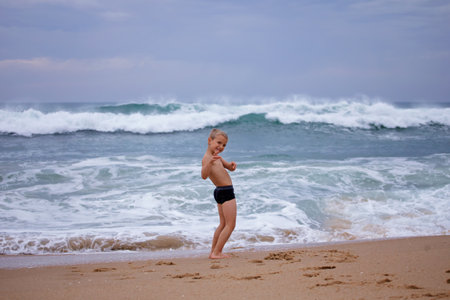 Little boy plays on the shore of a huge raging ocean. He joyfully runs away from the waves. Freedom, security, childhood. Challenge, adventure and travelの写真素材