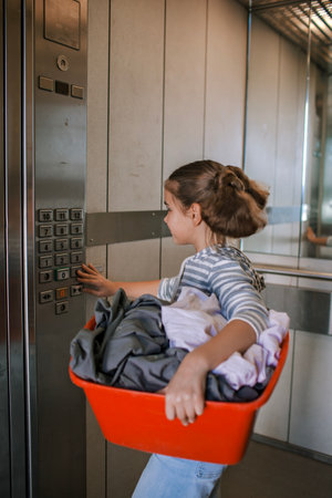 Teenage girl with a laundry basket going to common laundry. Concept of ecology, sustainability, care for environment, as well as saving money and natural resourcesの写真素材