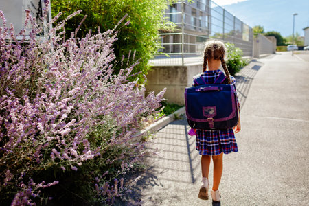 Back to school. Happy girl with backpack, primary school kids, going to school at the first day, study and education, return after vacations, lifestyle, back view, full length photoの写真素材