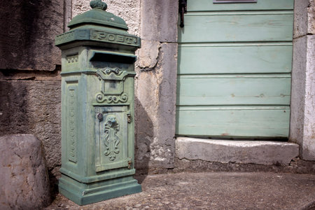An old-fashioned green mailbox by a weathered door with shutters, reflecting the charm of traditional European village post.の写真素材