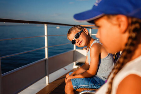 A boy wearing sunglasses and a blue cap relaxes on a boat with a girl, enjoying a sunny day on the water, embodying the joy of summer holidays.の写真素材