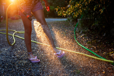 A playful moment captured as a child sprays water from a hose, the sunlight catching the mist against the evening backdrop, creating a summer scene of joy and refreshmentの写真素材