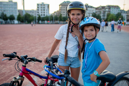 A boy and girl ride their bicycles together, smiling and enjoying the cityscape. The scene emphasizes energy, well-being, and the protective care provided by helmets during outdoor activities.の写真素材