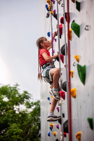 A confident child climbs a colorful bouldering wall with rope and harness. The image captures joy, courage, and coordination. Perfect for illustrating fitness, sport, and childhood challenge.の写真素材