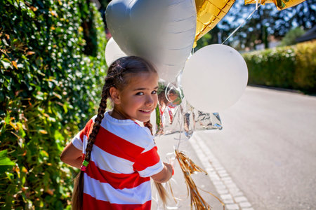 Close-up of a happy child smiling with colorful birthday balloons. Wind in her hair, sunset glow on her face. A candid celebration of innocence, joy, and youthful energyの写真素材