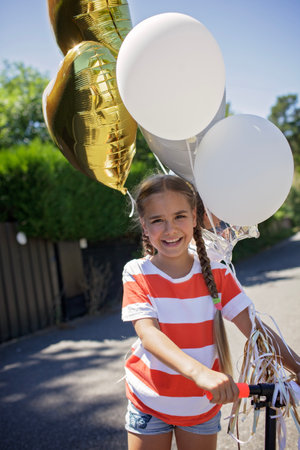 Close-up of a happy child smiling with colorful birthday balloons. Wind in her hair, sunset glow on her face. A candid celebration of innocence, joy, and youthful energyの写真素材