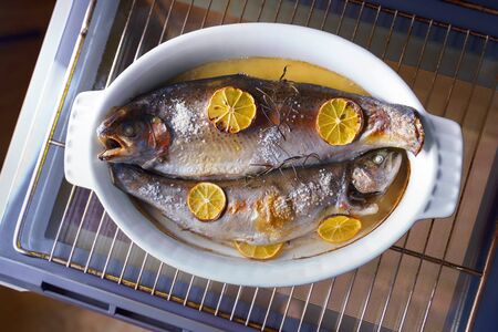 Flat lay two fishes with rosemary and lemon in white plate cooked homeの写真素材