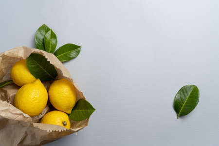 Lemons in craft paper with leaves on texture grey background with cope space. High quality photoの写真素材