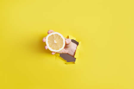 woman hand holding lemon through the hole in yellow paper . High quality photoの写真素材