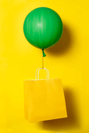 Big green ballon holding yellow package for delivery or present on yellow background. Non contact delivery. High quality photoの写真素材