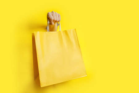 Woman hand holding yellow paper bag on yellow background . High quality photoの写真素材