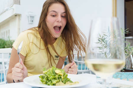 young pretty girl eat salad with funny face in yellow t-shirt. High quality photoの写真素材