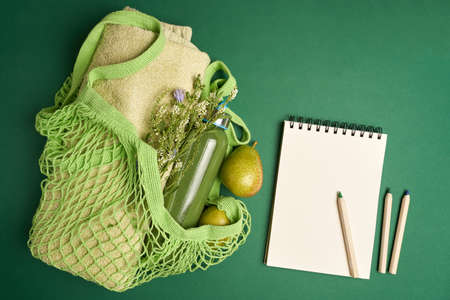 Green string bag with fruits, bath towel, glass bottle with smoothy, paper notepad and pencils on green background. High quality photoの写真素材