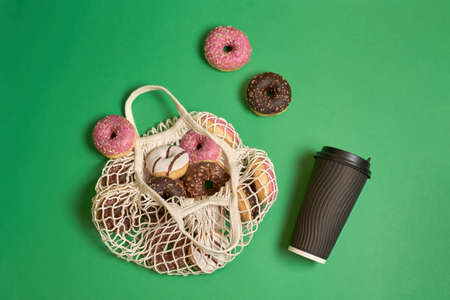 Donuts pink, brown, white in eco string bag and paper cut with coffee or tea on green background . High quality photoの写真素材