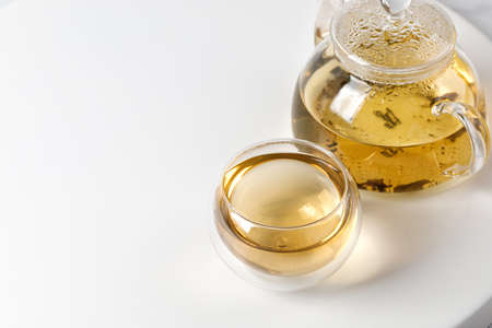 A glass of green herbal tea and glass teapot with tea leaves on white background. Double Wall Glass Cupの写真素材