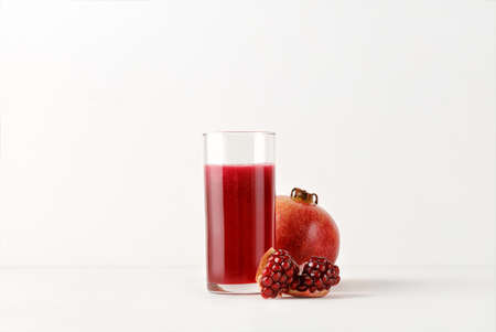 Fresh pomegranate juice in glass with fresh pomegranate fruits on white background for menu and mock up. perfect and minimalistの写真素材