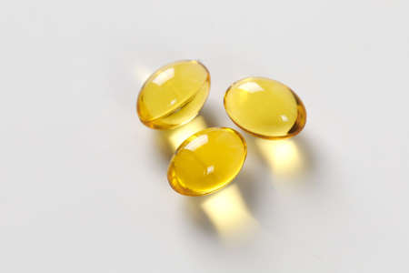Three yellow pills. Omega, vitamin D, Close up. Macro vitamins on white table