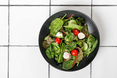 Plate of Fresh green salad on tile background. Mix of salad leaves with cucumber, cherry tomatoes, mozzarella. top viewの写真素材