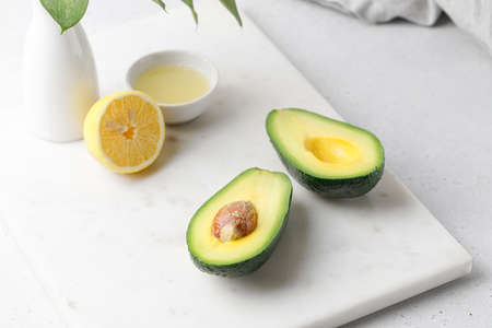 Cut ripe green avocado on a white marble board with vase and lemon juice on gray background. food...